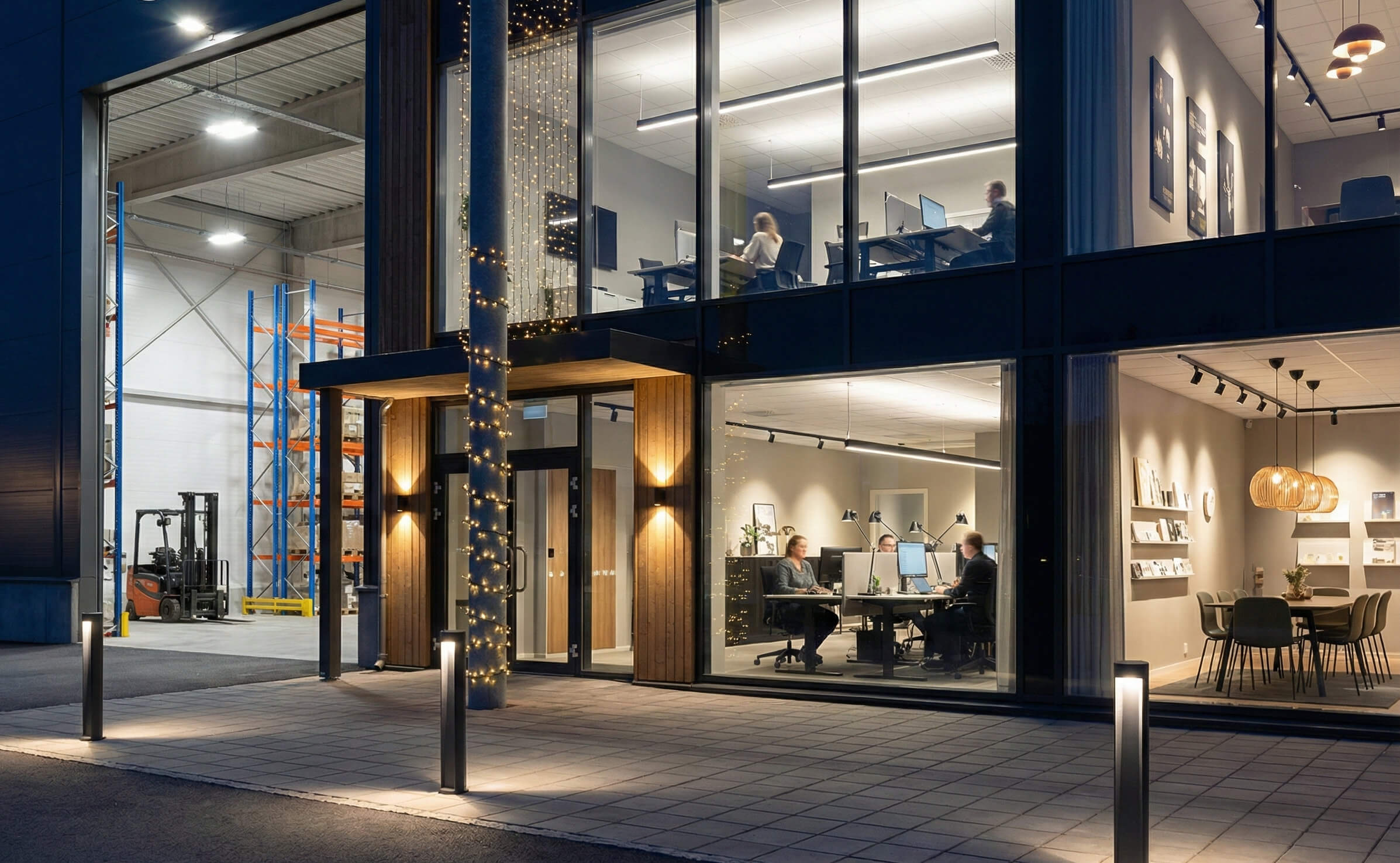 Rätt ljus för varje yta. Denna bild visar exempel på en komplett belysningslösning. Från kraftfulla industriarmaturer i lagret (t.v.) och ergonomisk kontorsbelysning med linjära pendlar och paneler (t.h.), till trygghetsskapande pollare och fasadljus utom LjuslingorKvällsbild av en modern fastighet som visar olika belysningsprodukter installerade. I förgrunden syns tända pollare längs en gångväg och väggarmaturer som lyser upp fasaden. Inne i kontorsdelen till höger syns nedpendlade linjära armaturer, infällda takpaneler samt en del dekorativ belysning. Till vänster genom en stor port syns ett lager upplyst av kraftiga, höghängande industriarmaturer (high-bay).